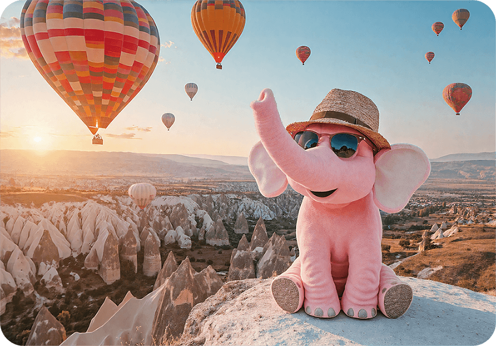 Tiny the elephant wearing sunglasses and a hat with hot air balloons in the background.